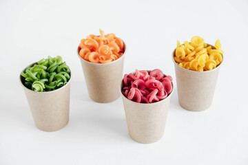 Multicolored pasta in a disposable kraft paper cups on a white background. Top view. Copy, empty space for text