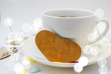 on a white saucer with a Cup of coffee is a wooden heart. Light background with bokeh. Space for text