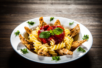 Roast chicken nuggets with fusilli and tomato sauce on wooden table
