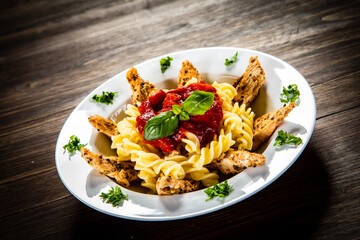 Roast chicken nuggets with fusilli and tomato sauce on wooden table
