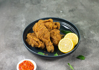 Close up view of fried chickens with golden shiny, crispy and oily textured. Served on ceramic grey plate with chili sause, garnished with basil leaves and lemon slices. Grey  wooden background.