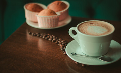 Coffee on wooden table close up in coffee shop , coffee beans and cupcakes around it