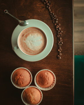 Coffee On Wooden Table Close Up In Coffee Shop , Coffee Beans And Cupcakes Around It