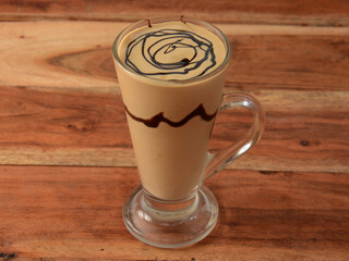 Thick cream cold coffee in a tall glass with cream poured on a old rustic wooden table.