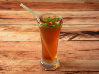 Traditional iced tea in a glass with mint and paper straws on a rustic wooden background.