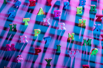 Alphabet letters in random order. Multi-colored letters are on table. Pink background.  Letters are...
