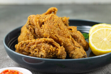 Close up view of fried chickens with golden shiny, crispy and oily textured. Served on ceramic grey plate with chili sause, garnished with basil leaves and lemon slices. Grey  wooden background.