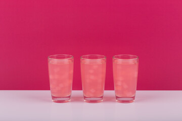 Three pink cocktail shots on white table against pink background