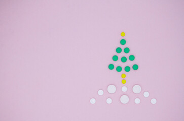 White , yellow and green medical pills in the form of a Christmas tree in the snow on a pink background. Christmas medical flatly. Copy space.
