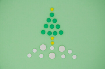 White , yellow and green medical pills in the form of a Christmas tree in the snow on a green background. Christmas medical flatly.