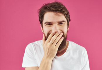 Portrait of a happy guy in a white T-shirt with a thick beard on a pink background