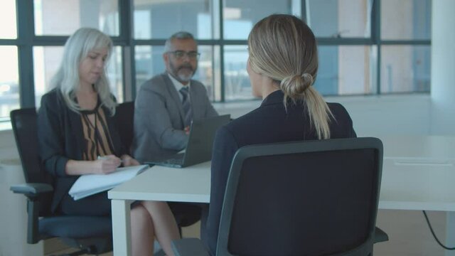 Female job candidate meeting and talking to employer and HR manager, sitting at table at speaking. Back view. Job interview and career concept