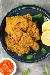 Close up view of fried chickens with golden shiny, crispy and oily textured. Served on ceramic grey plate with chili sause, garnished with basil leaves and lemon slices. Grey  wooden background.