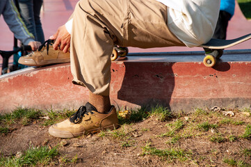 a teenager sits on a skateboard and ties his shoelaces on sneakers. High quality photo