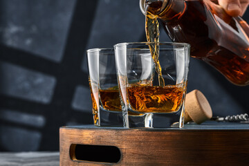 Two square glasses of whiskey with ice on a tray, the glass is filled with whiskey from the bottle.