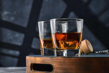 Two square glasses of whiskey with ice on a wooden tray, on a blue background.