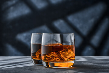 Two glasses of whiskey with ice on a concrete table on a blue background.