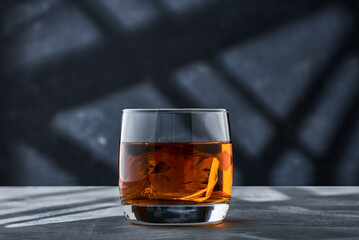 Round glass of whiskey with ice on a concrete table on a blue background.