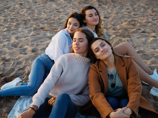 Fototapeta premium Group of young women on a picnic on the beach, enjoying the sunset. Meeting friends,