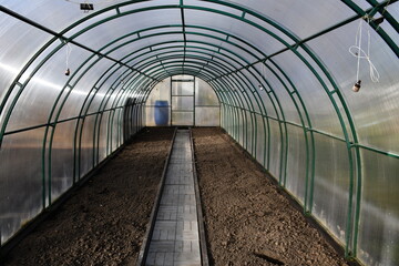 Freshly dig up empty beds in a greenhouse of polycarbonate. The track is lined with tiles. Neat beds.