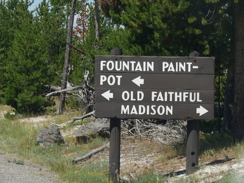 Directional wooden sign with arrows pointing to the directions to the Fountain Paint Pot, Old Faithful and Madison at Yellowstone National Park.
