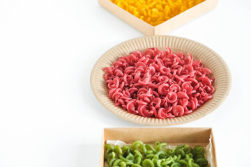 Multicolored pasta in a disposable kraft paper plates and boxes on a white background. Top view. Copy, empty space for text