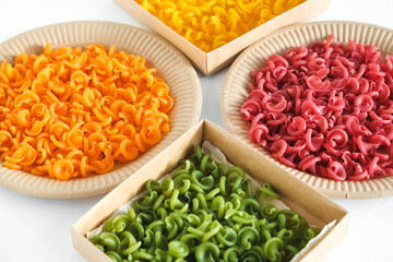 Multicolored pasta in a disposable kraft paper plates and boxes on a white background. Top view. Copy, empty space for text