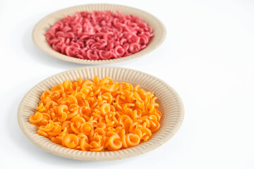 Orange and red pasta in a disposable paper plate on a white background. Top view. Copy, empty space for text