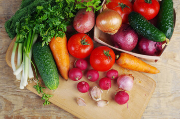 Appetizing vegetables, tomatoes, cucumbers, carrots, onions, garlic, peppers, radishes on a wooden table.