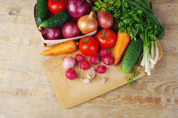 Appetizing vegetables, tomatoes, cucumbers, carrots, onions, garlic, peppers, radishes on a wooden table.