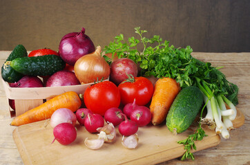 Appetizing vegetables, tomatoes, cucumbers, carrots, onions, garlic, peppers, radishes on a wooden table.