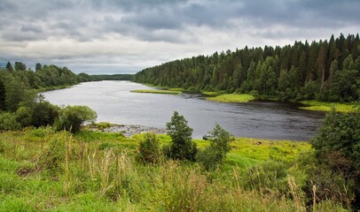 Fototapeta na wymiar Turning Onega river with quick stream surrounded with thick green forest in summer against cloudy sky in Arkhangelsk region, Russia.