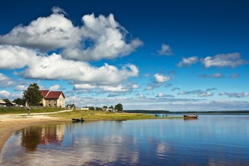 The view on the house on the sandy bank of the transparent lake with boats against cloudy sky in Kenozersky National Park, Arkhangelsk region, Russia.
