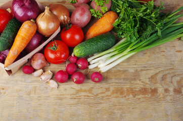 Appetizing vegetables, tomatoes, cucumbers, carrots, onions, garlic, peppers, radishes on a wooden table.