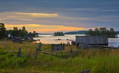 Fototapeta na wymiar Rural area in summer in North Karelia, Russia. Small wooden houses on the bank of the White sea against colorful sunset.