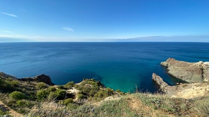 Fototapeta na wymiar Panoramic seascape - calm azure sea, horizon, rocks and mountains surround the Black Sea bay in Crimea, Cape Fiolent in Sevastopol.
