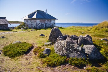 A brick small house on the grassy shore of the White sea and huge cobbles in the foreground on Solovetsky Islands, Russia.
