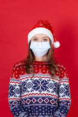 Fototapeta na wymiar young woman in medical mask, Santa Claus hat and patterned sweater isolated on red background.