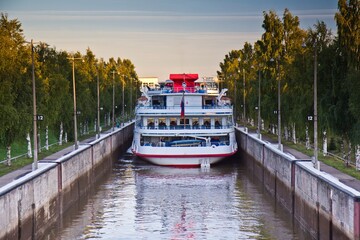 Fototapeta premium A ferry ship full of passengers in the lock of Volga-Baltic Canal and growing trees along it in Vytegra, Vologda Oblast, Russia.