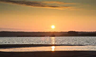 The view on sunset at the beach of the Northern Dvina river, a ship and a barge floating  and forests in the background in Russia.