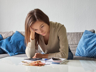 Fototapeta na wymiar A young, depressed, stressed woman props her head with her hand. Pensive, broken and sad girl bends over the bills. There is euro money and a calculator on the table
