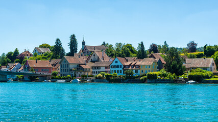 Petit village de maisons traditionnelles devant un lac en Suisse par une journée ensoleillée avec des arbres et de la verdure à l'arrière plan