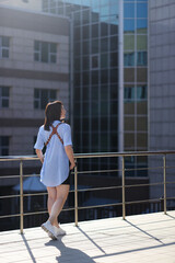 modern photographer happy girl in a leather cut for the camera against the backdrop of skyscrapers. woman wearing a blue shirt, black shorts and white trendy sneakers