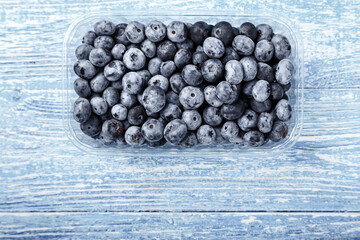 Blueberries in a plastic container on a wooden table. Space for text.