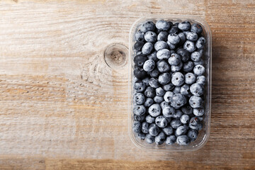 Blueberries in a plastic container on a wooden table. Space for text.