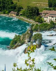 Fototapeta na wymiar Panorama des cascades du Rhin ou Rheinfall en Suisse par une journée ensoleillée avec un ciel bleu avec les rochers et un village et les embruns du fleuve.