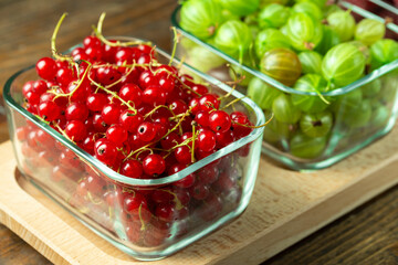 Fresh berries of gooseberries, raspberries and red currants in a glass dish on a wooden table. The concept of healthy food