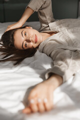 Vertical shot of smiling young woman lying in bed, looking at camera happy. Concept of wellbeing and leisure