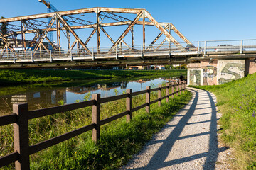 Obraz premium Pathway, foot path next to a river leading under a brige, in calm suburbian town a sunny summer day, out running, walking traveling, 