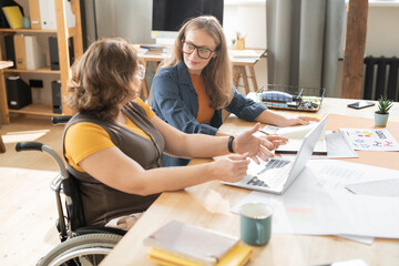 Two young female office managers sitting by table and discussing working points